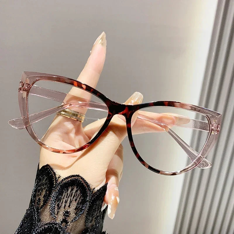Eine Hand hält eine rosa-klare Vintage Cat-Eye-Brille mit braun-schwarz gemusterten Linsen.