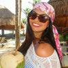 A smiling woman wearing a pink floral satin shawl and a white lace top holds a green apple outdoors.