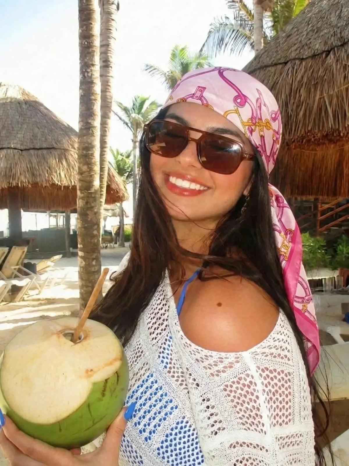 A smiling woman wearing a pink floral satin shawl and a white lace top holds a green apple outdoors.