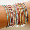 A stack of colorful beaded bangles worn on a wrist, featuring shades of pink, orange, green, and blue.