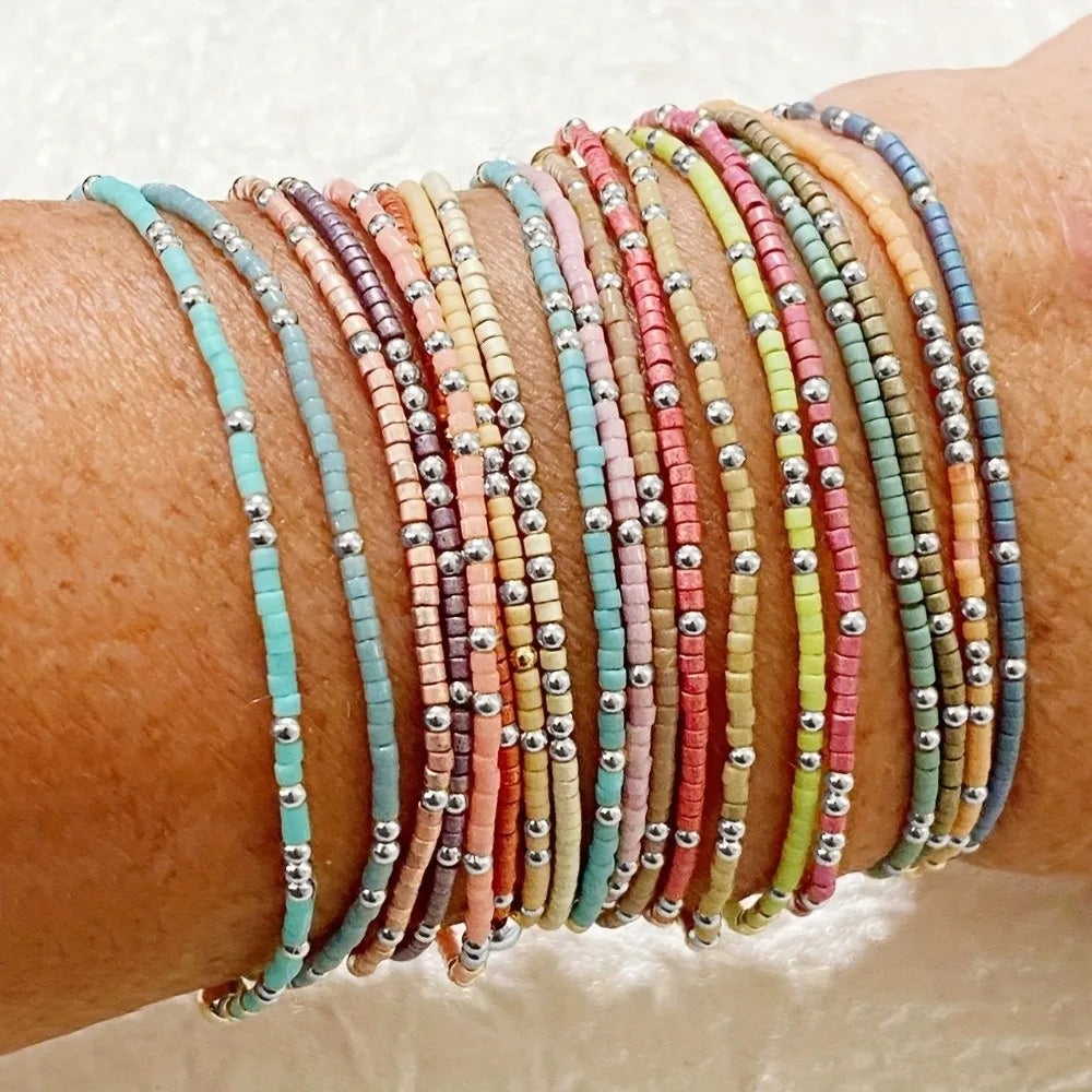 A stack of colorful beaded bangles worn on a wrist, featuring shades of pink, orange, green, and blue.