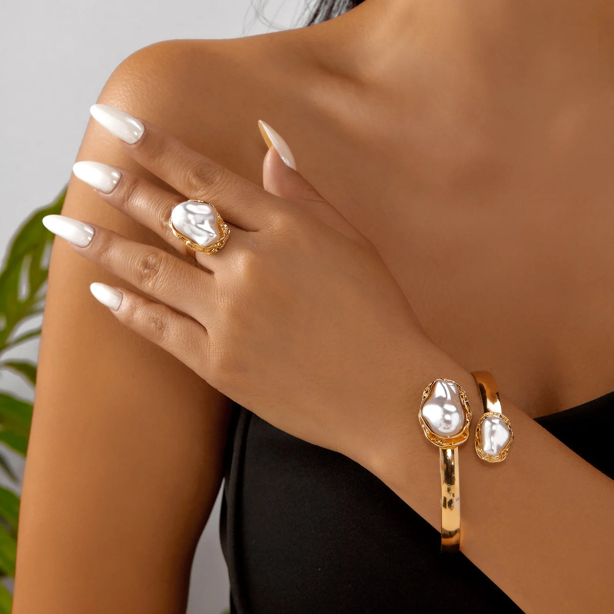 A close-up of a hand wearing a gold baroque imitation pearl jewelry set including rings and bracelets.