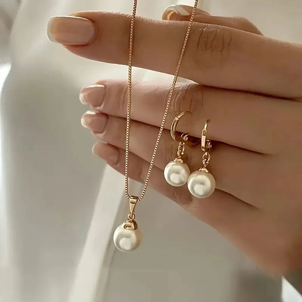 A hand models a dainty pearl jewelry set featuring matching earrings and a delicate necklace.