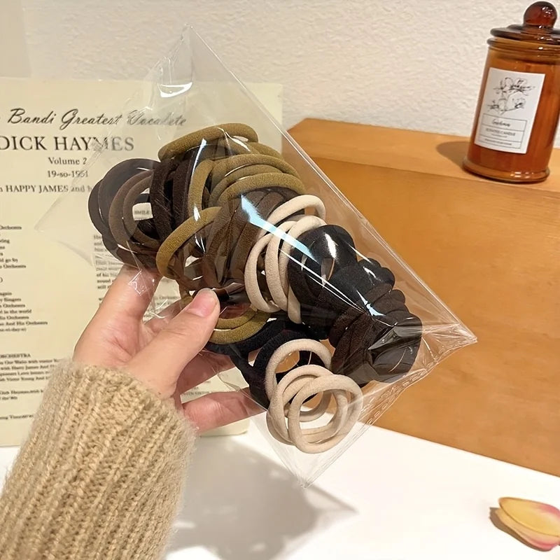 A hand holds a clear plastic bag filled with various brown and black boho seamless elastic hair ties.