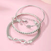 A set of three silver-toned crystal heart charm bracelets displayed on a pink background.