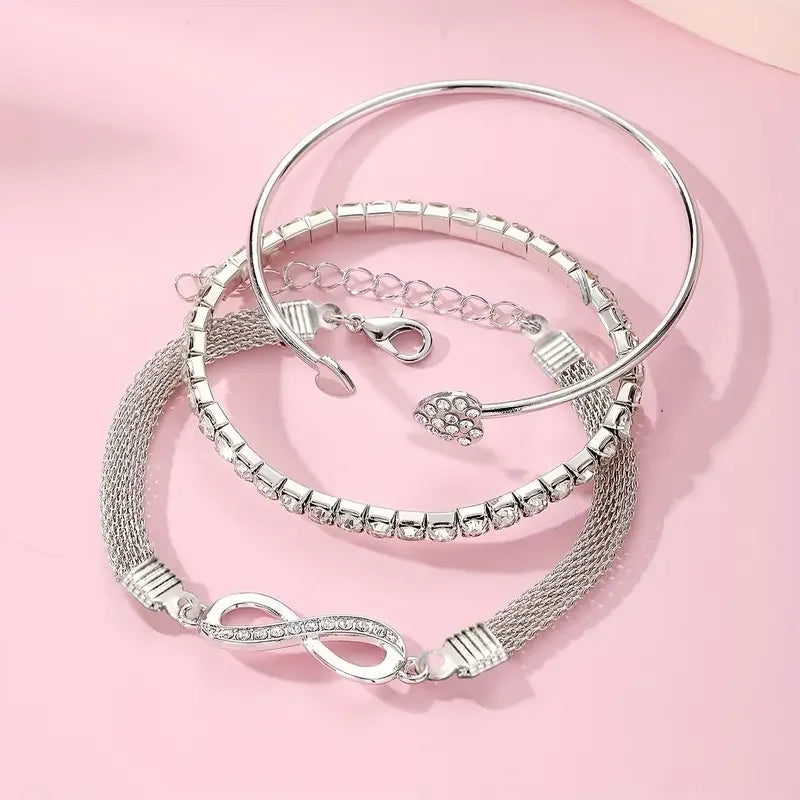 A set of three silver-toned crystal heart charm bracelets displayed on a pink background.
