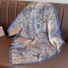 A flowing silk scarf with a delicate floral and paisley print in shades of blue, beige, and gold draped over brown leather fu