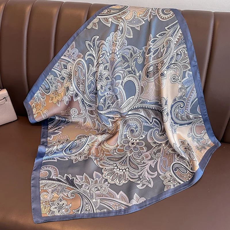 A flowing silk scarf with a delicate floral and paisley print in shades of blue, beige, and gold draped over brown leather fu