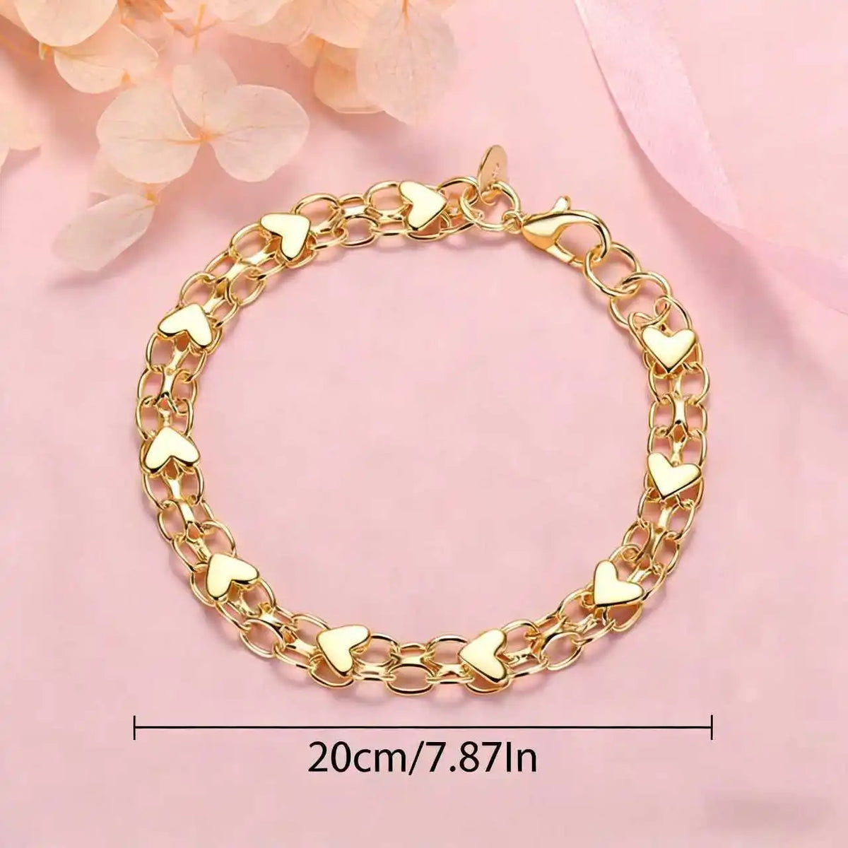 Gold heart charm bracelet made of 925 sterling silver for women displayed on a pink background