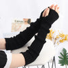 A close-up of black knitted fingerless gloves being worn on a hand, displayed against a white background.