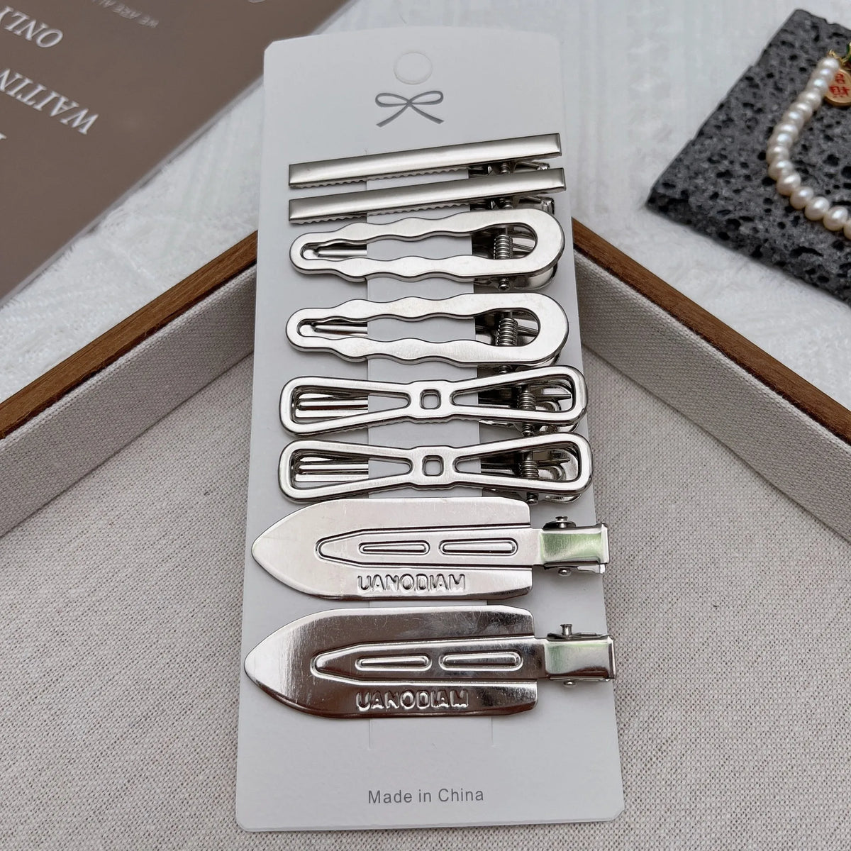 Un juego de ocho clips metálicos para flequillo y accesorios para el cabello, mostrados en una caja de color gris claro.