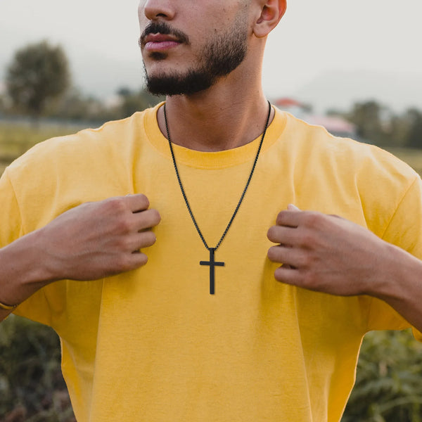 A man wearing a yellow t-shirt is displaying a black stainless steel cross necklace.