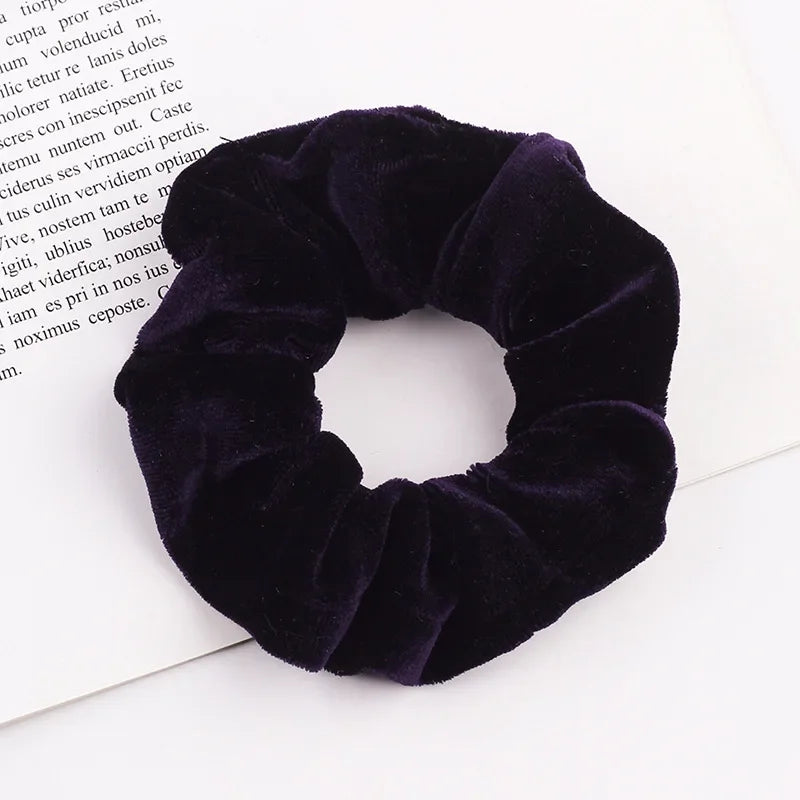 A dark purple velvet scrunchie is shown against a white background.