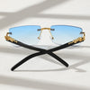 A pair of trendy frameless rectangular sunglasses with blue lenses and gold accents resting on a white surface.