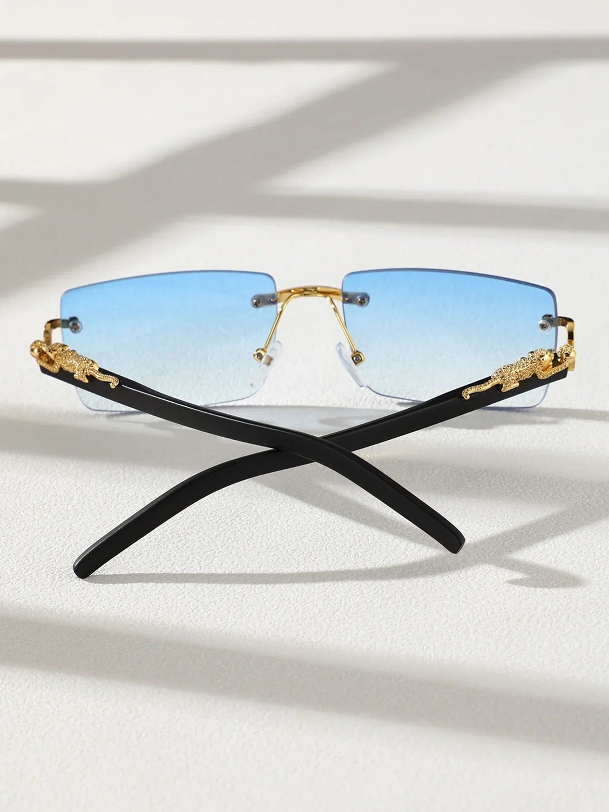 A pair of trendy frameless rectangular sunglasses with blue lenses and gold accents resting on a white surface.