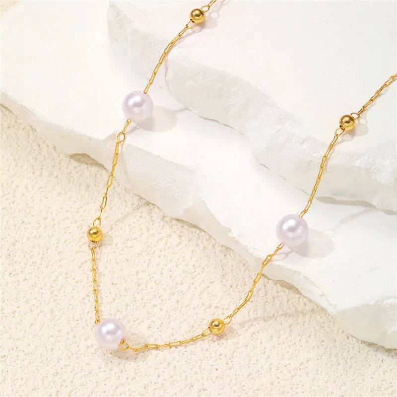 Un délicat collier en or avec des charms de perles et de billes d'or sur une surface de pierre blanche.