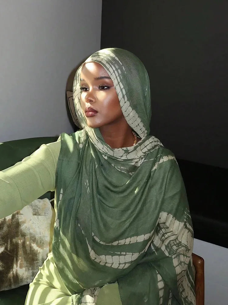 امرأة ترتدي حجابًا أخضر بنقشة جلد التمساح، جالسة في الداخل.
