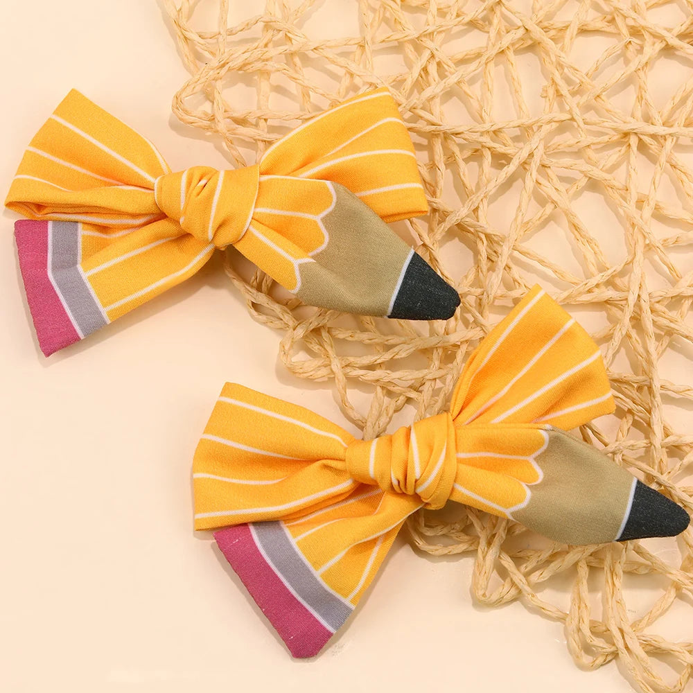 A set of cute pencil bow hair clips in yellow and gray fabric laid on a natural fiber mat.