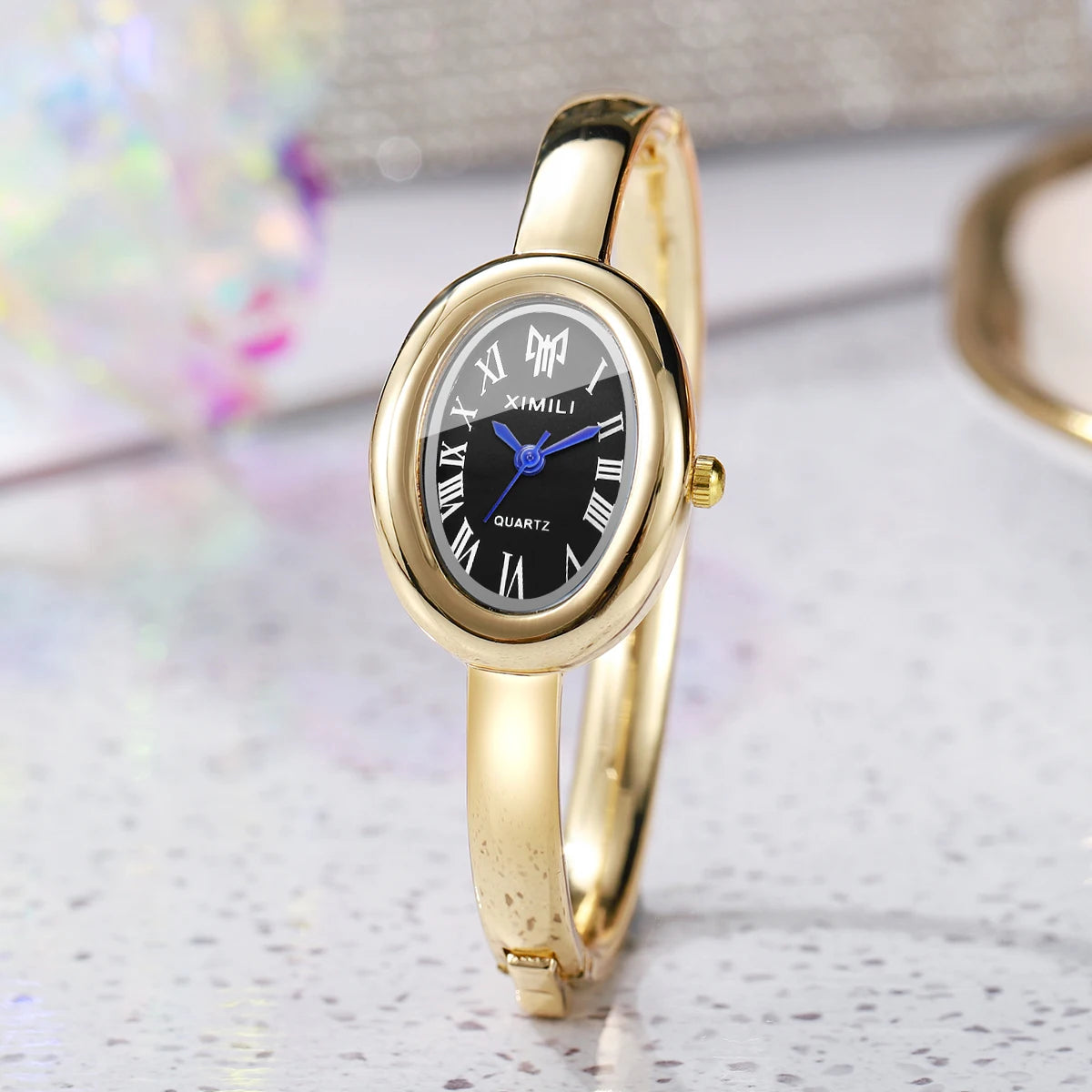 A gold-toned quartz watch bracelet with a round face and Roman numerals is displayed on a white surface.