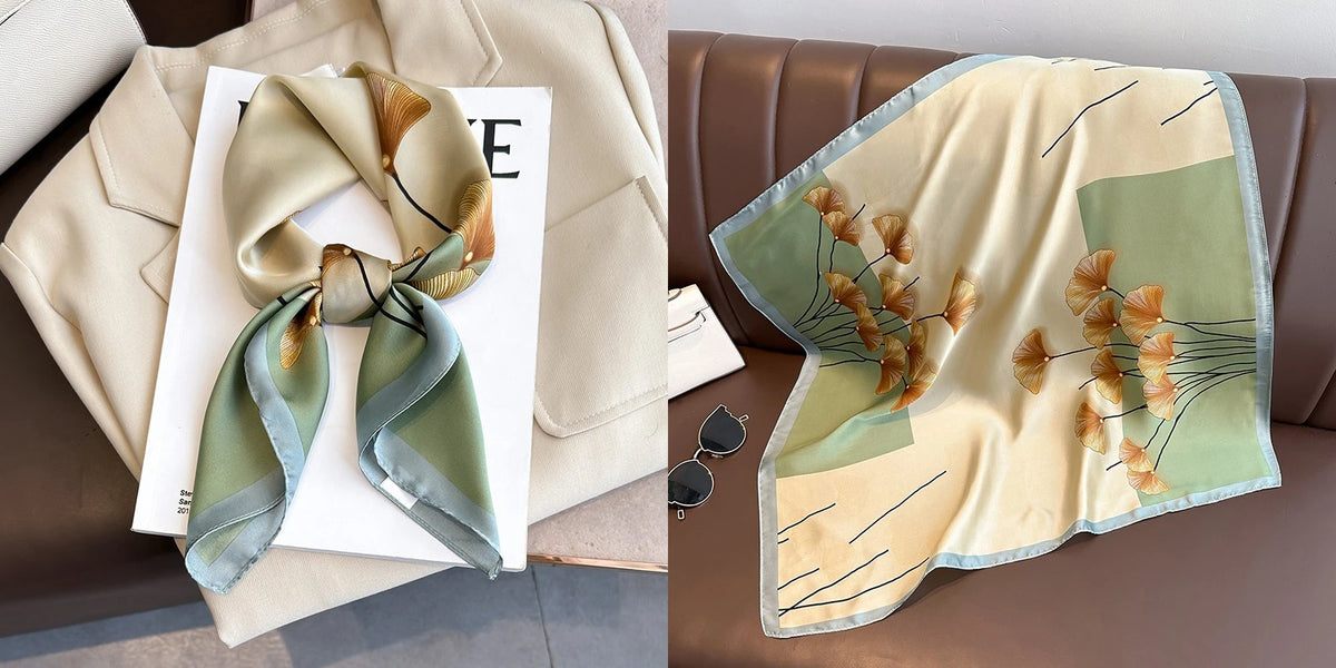 A silk scarf with a floral print in muted green and beige tones is displayed on a light background.