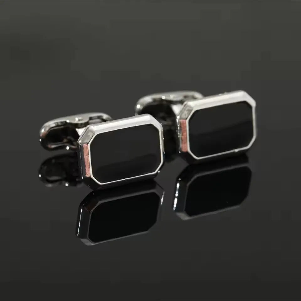 Une paire de boutons de manchette carrés rayés classiques pour hommes, posés sur une surface sombre et réfléchissante.