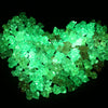 A pile of luminous glow-in-the-dark acrylic beads showing various shades of green light.