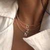 A close-up of a delicate rose gold crystal necklace featuring the initial DNZ charm worn against a white shirt.