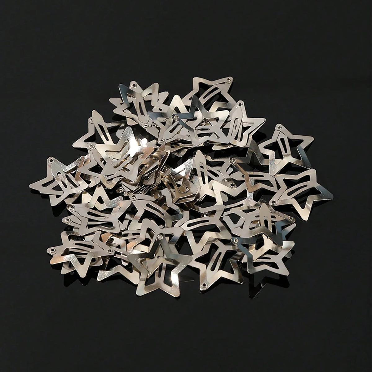 A pile of silver star-shaped metal snap hair clips scattered on a dark surface.