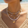 A close-up of a woman wearing a layered necklace featuring pearls and a gold starfish pendant.