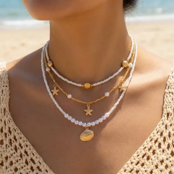 A close-up of a woman wearing a layered necklace featuring pearls and a gold starfish pendant.