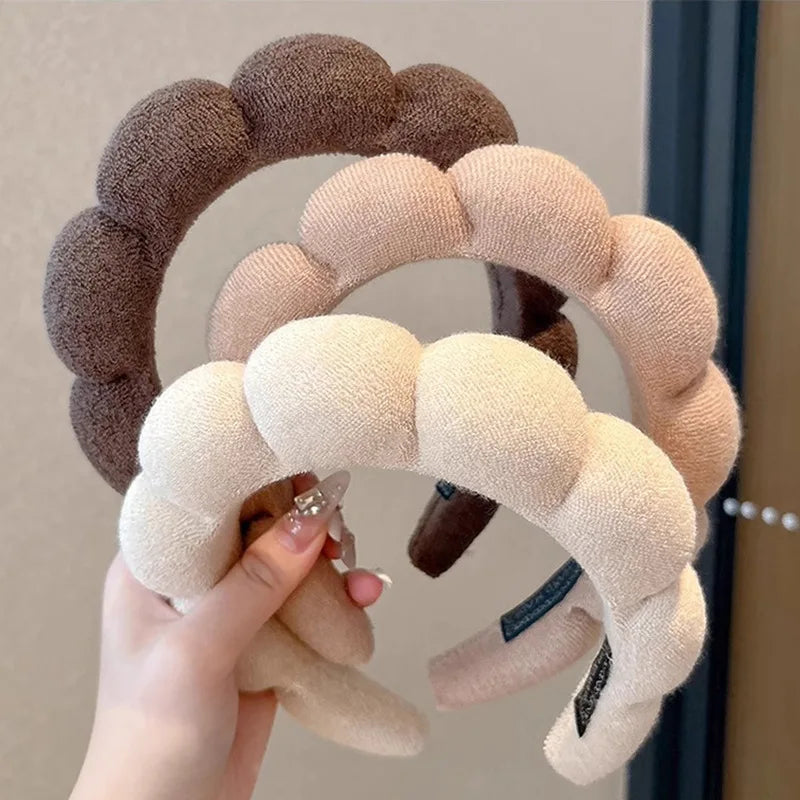 A hand holds a beige cloud sponge hair accessory headband with brown accents.