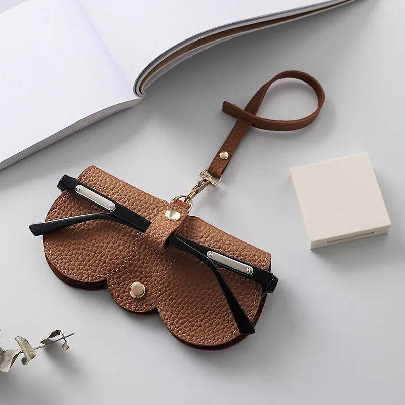 A brown leather pouch with a strap and metal accents is shown next to a white box on a light gray surface.