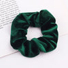 A close-up of a dark emerald green velvet scrunchie with gathered fabric texture.