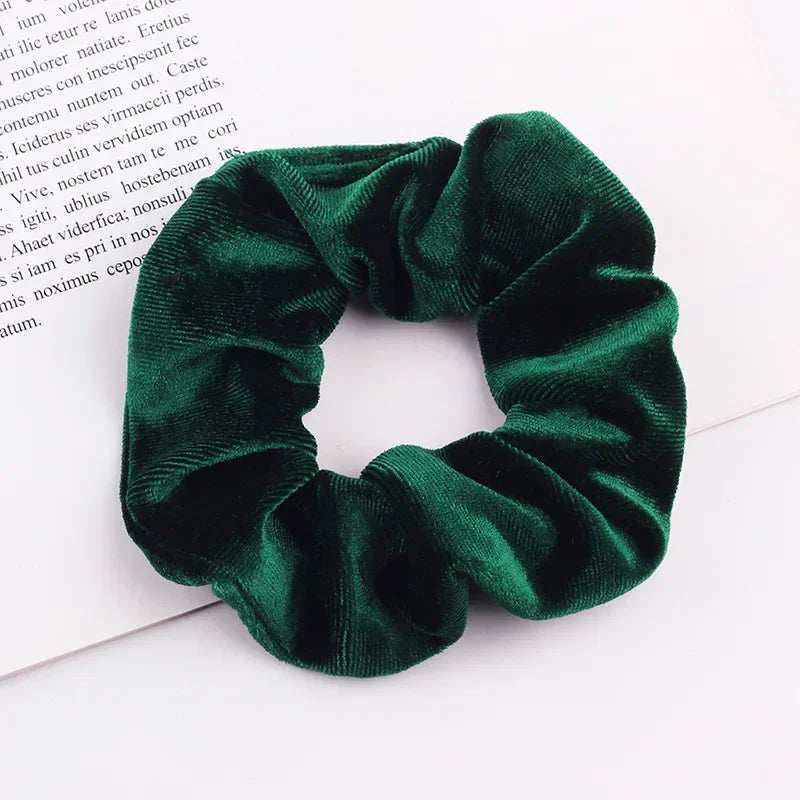 A close-up of a dark emerald green velvet scrunchie with gathered fabric texture.
