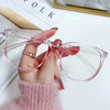 A hand holds a pair of pink, clear-framed anti-blue light spectacles against a white background.