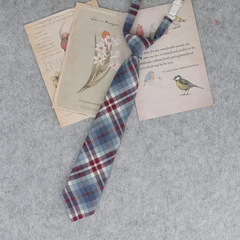 A plaid necktie featuring a blue and red tartan pattern, displayed alongside vintage-style paper with illustrations.