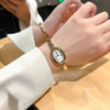 A close-up of a woman's hand wearing an elegant vintage quartz analog watch with an oval face on a light-colored sleeve.