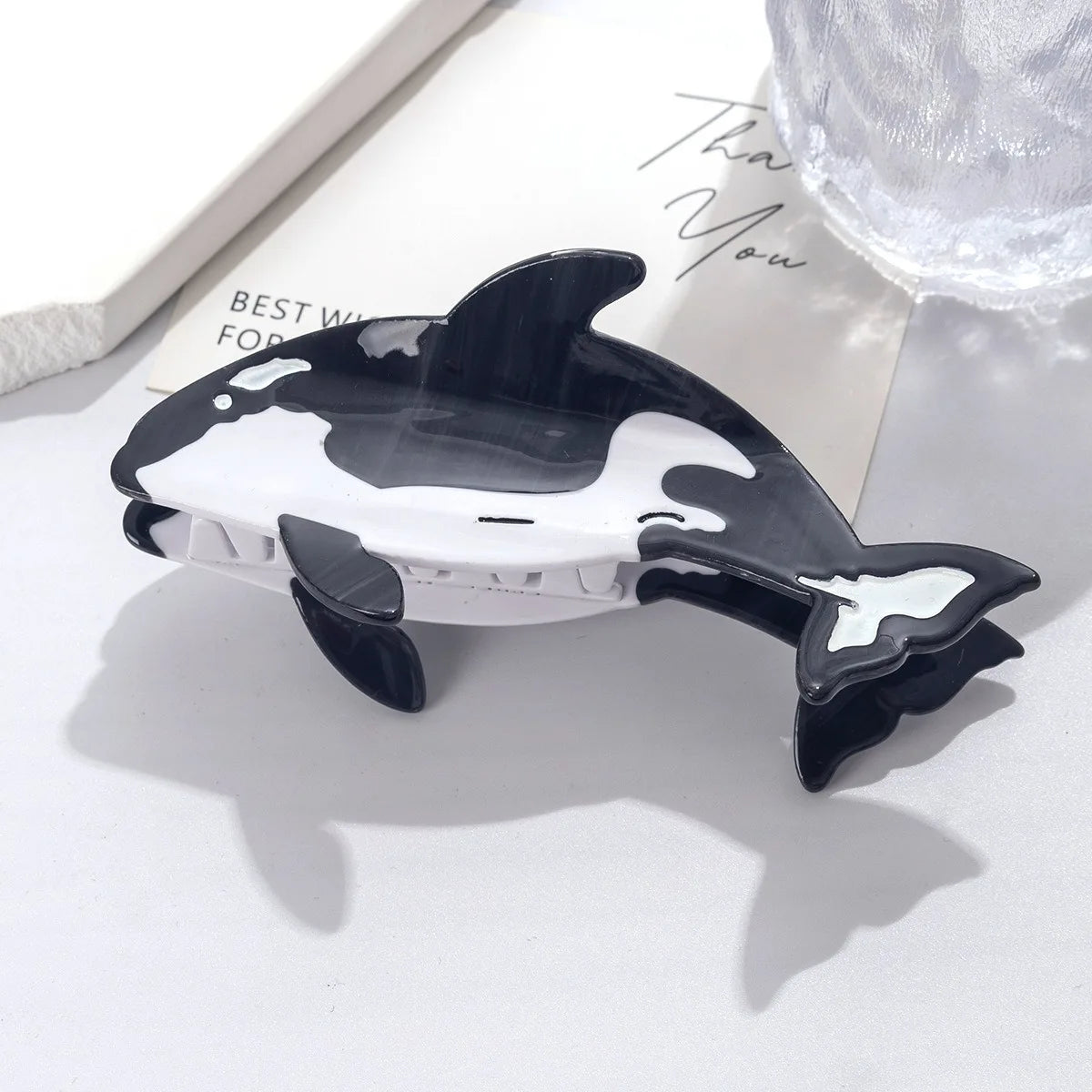 Pinza para el pelo con forma de delfín, temática de vaca en blanco y negro, sobre una superficie blanca.