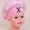 Pink sleep cap for kids with a ruffled crown and a black letter X detail