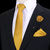 Chaqueta negra con camisa blanca y corbata de seda dorada, pañuelo de bolsillo dorado y prendedor floral dorado.