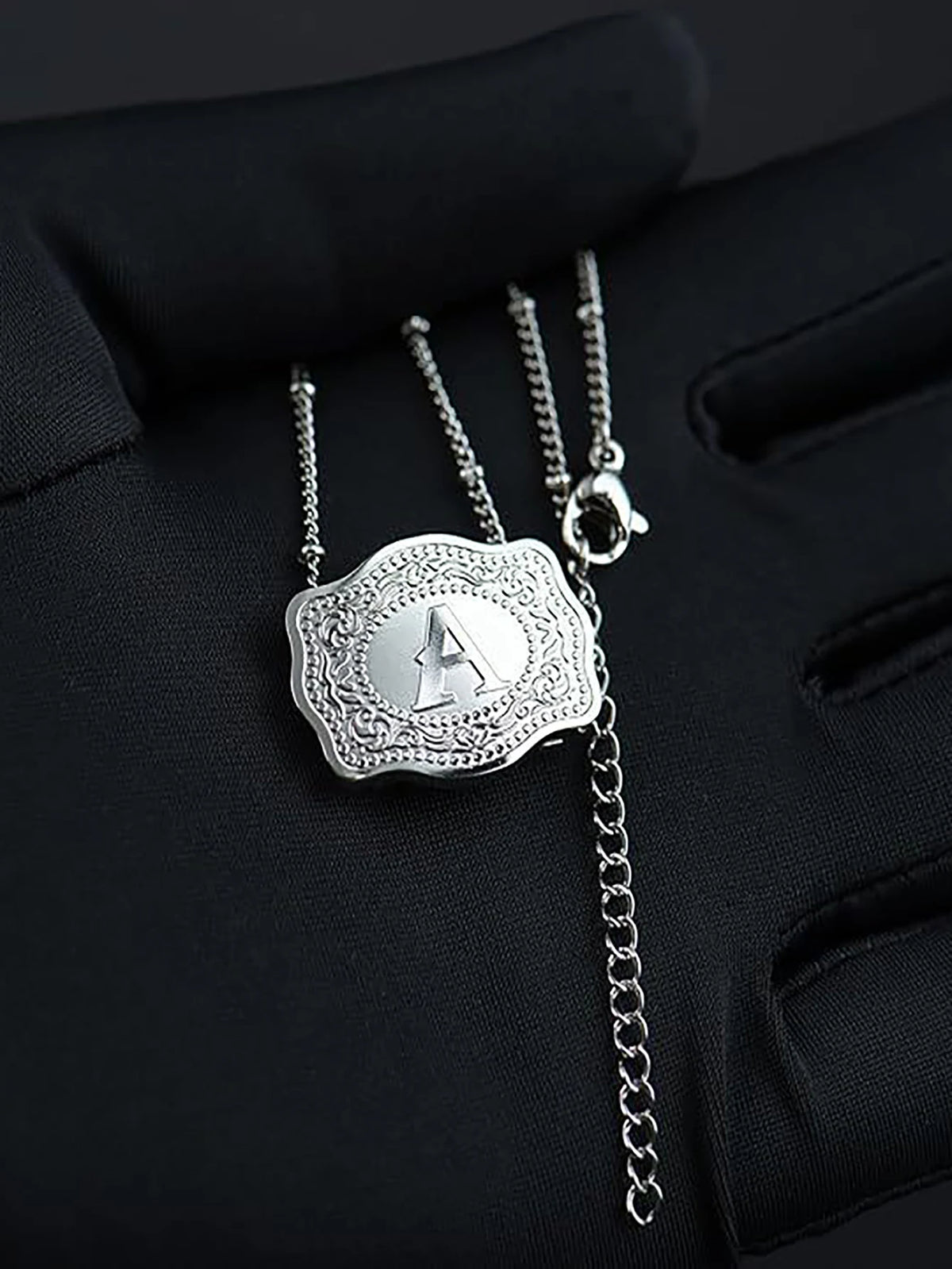 Silver initial letter pendant necklace with a chain displayed on a black glove.