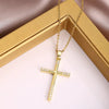 A dainty gold cross charm necklace with small diamonds displayed on a light pink velvet box.