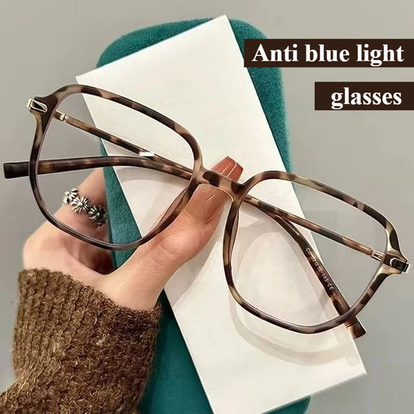 A pair of brown tortoiseshell anti blue light glasses resting on a white card against a teal background.