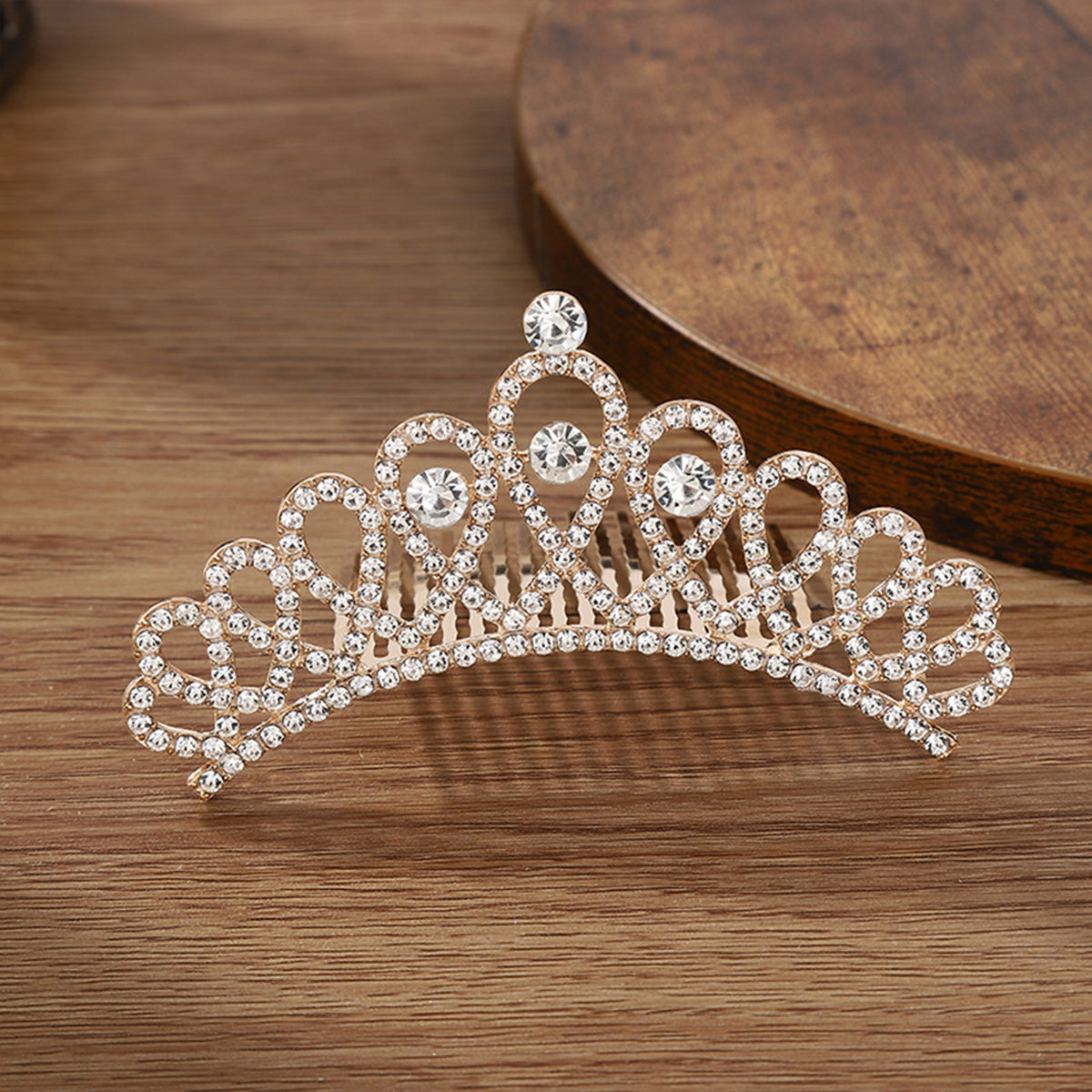 A sparkling crystal princess tiara hair comb for women displayed on a wooden surface.