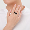 A hand wearing a black silicone wedding band on the ring finger, against a white shirt background.