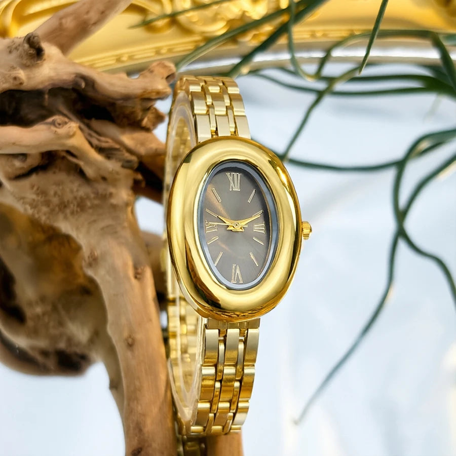 Primer plano de un reloj vintage dorado con correa de cuero junto a una rama de madera y follaje verde.