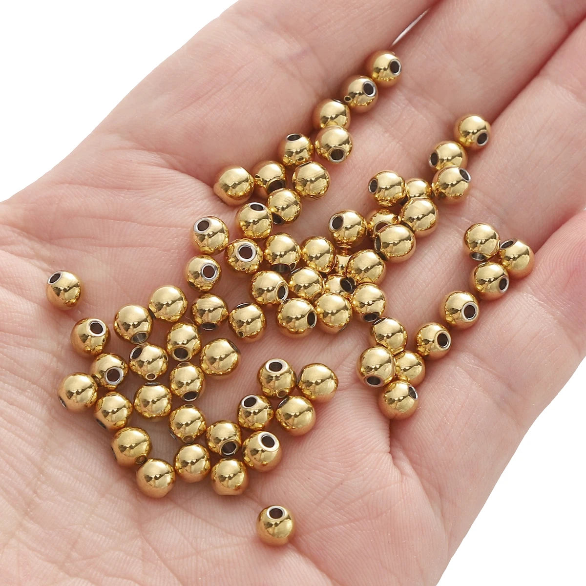 A hand holds a cluster of small gold-colored stainless steel spacer beads for DIY jewelry making