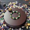 A natural stone and wooden bead prosperity bracelet displayed on a dark brown wooden stand surrounded by various colorful sto