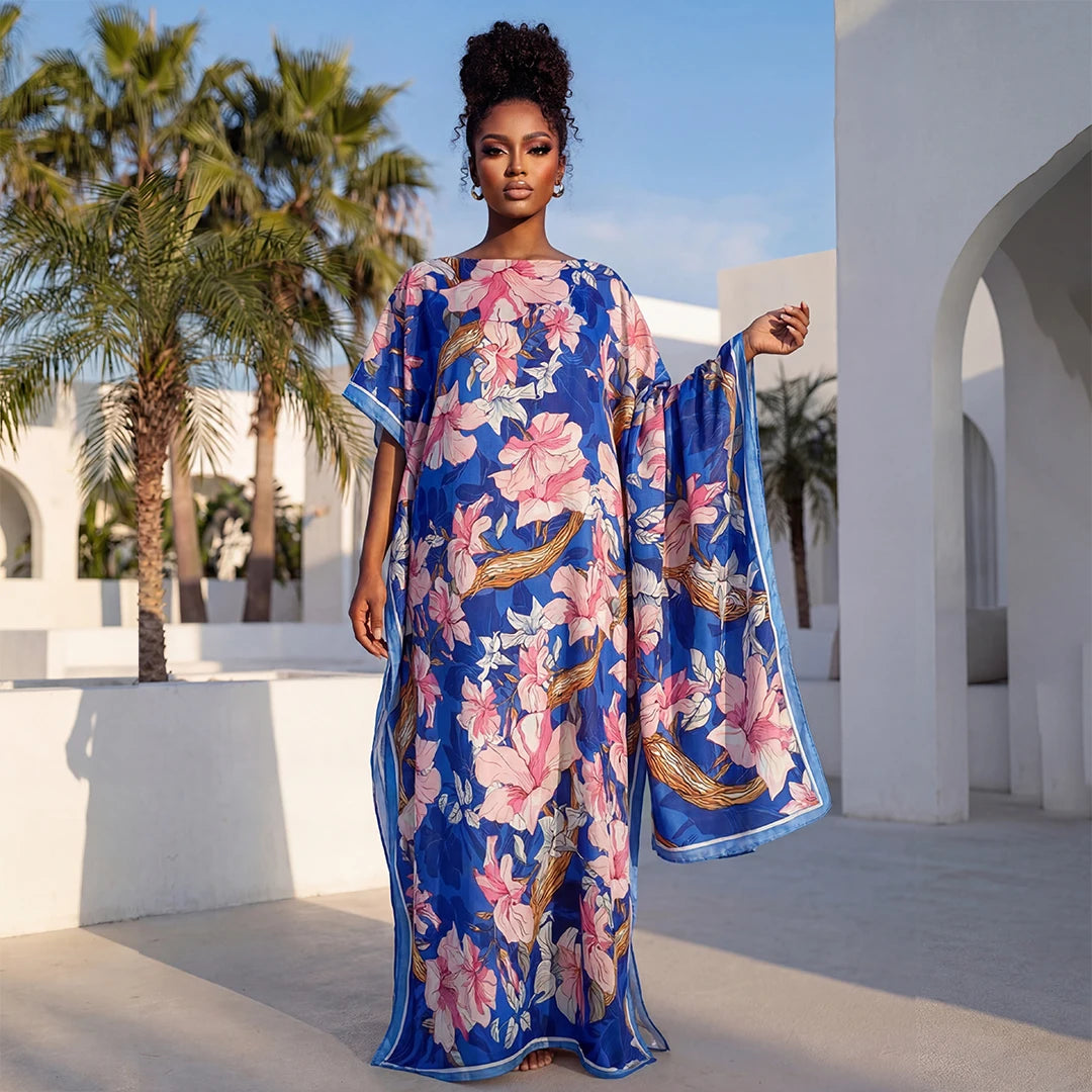 Une femme modélise une longue robe maxi florale bleue dans un cadre extérieur lumineux.