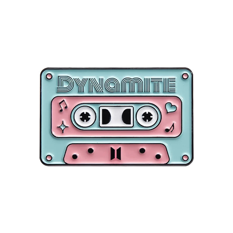 A vintage enamel pin featuring the word Dynamite and a cassette tape design in teal and pink.